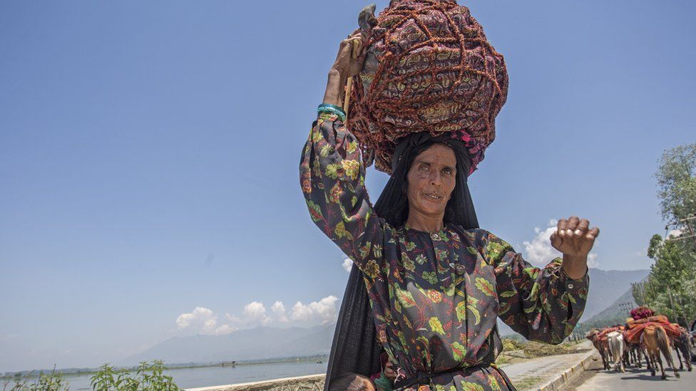 A shepherd woman poses a photograph as she carries her son and belongings near Dal lake