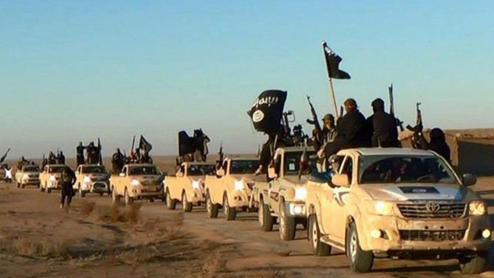 Islamic State militants hold up their weapons and wave flags as they ride in a convoy, which includes multiple Toyota pickup trucks, through Raqqa city in Syria