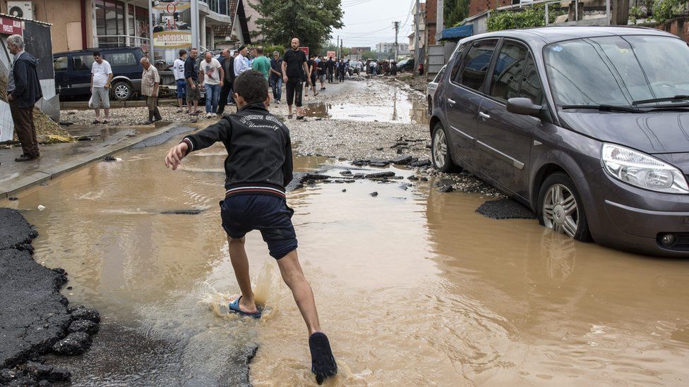 boy running through floodwater next to abandoned car in busy street