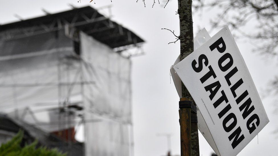 Polling station sign falling off a lamp-post