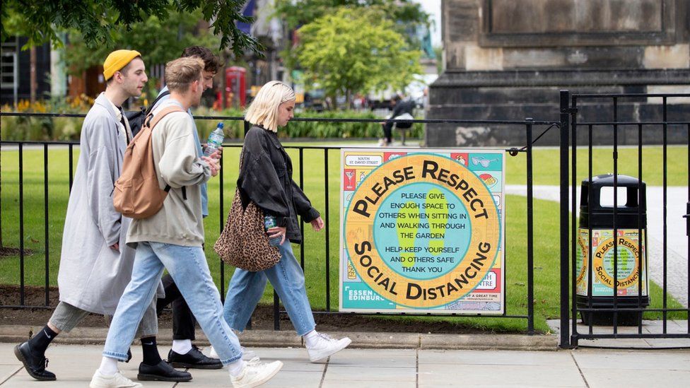 Edinburgh people walk past a sign advertising social distancing