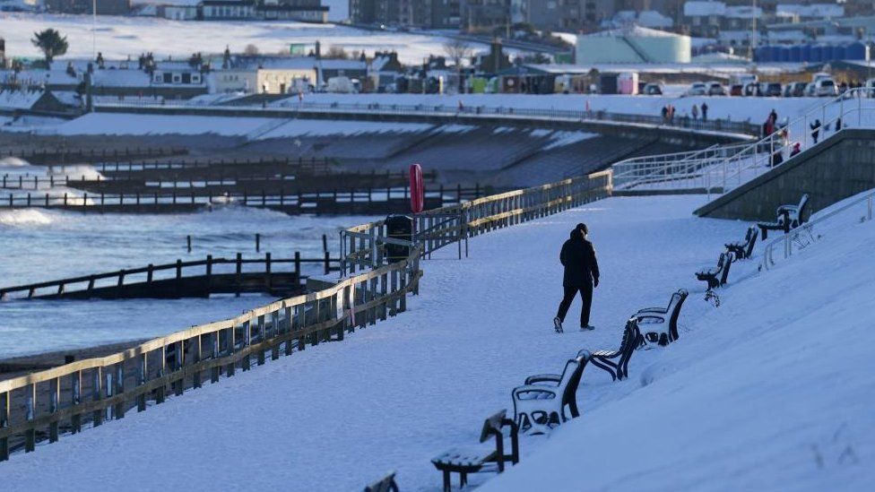 A person walks along a beach in Aberdeen which is covered in snow in January