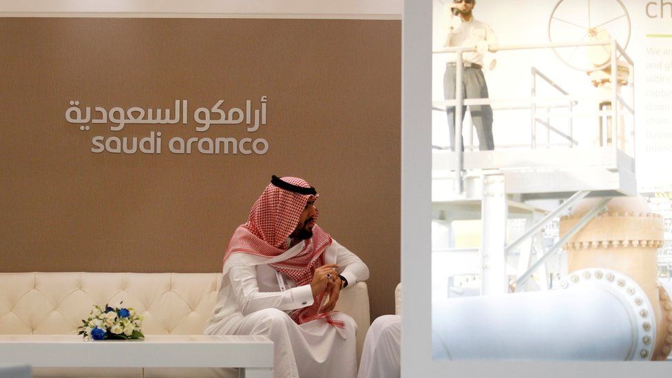 Man in Saudi dress by Saudi Aramco signage