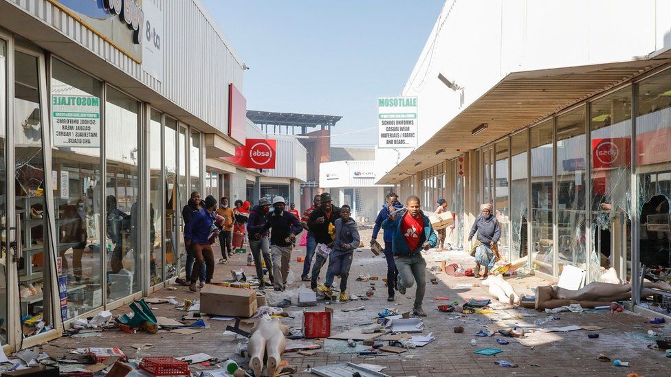 People flee from police as they carry goods while looting and vandalising the Lotsoho Mall in Katlehong township, East of Johannesburg, on July 12, 2021