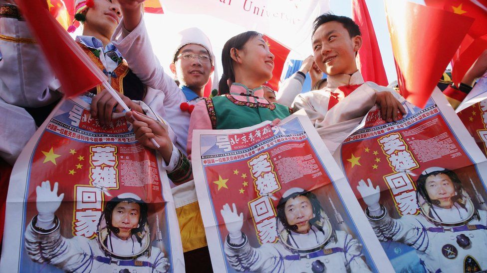 People hold up newspapers with the first Chinese man to go to space on the front page