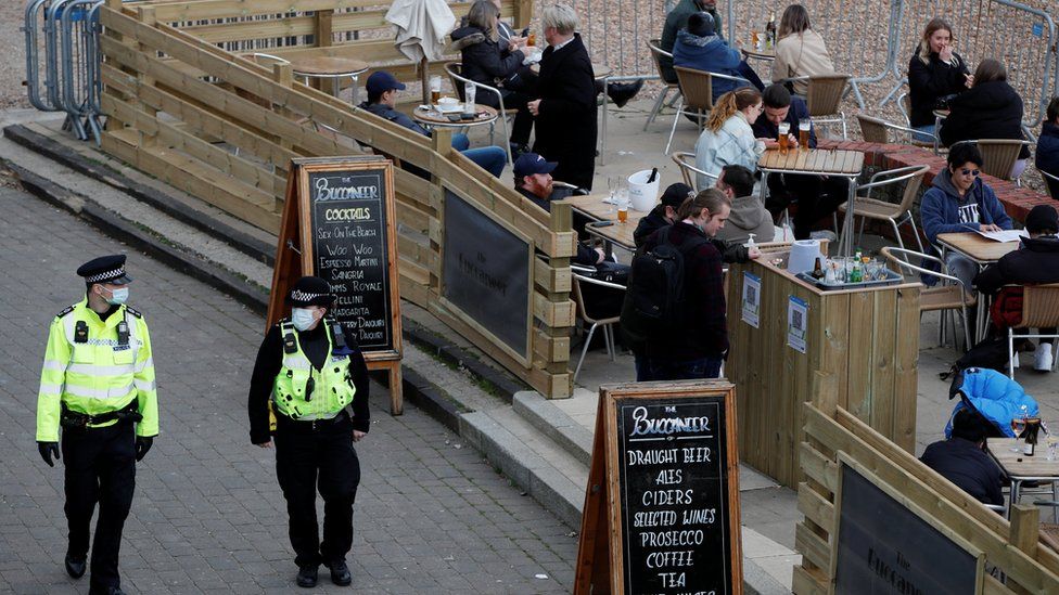 Police officers walk pass the terrace of a bar where people drink in Brighton after restrictions were eased on 12 April