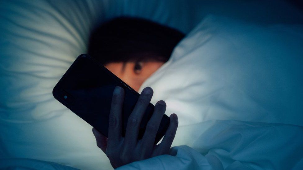Женщина листает телефон в постели ночью