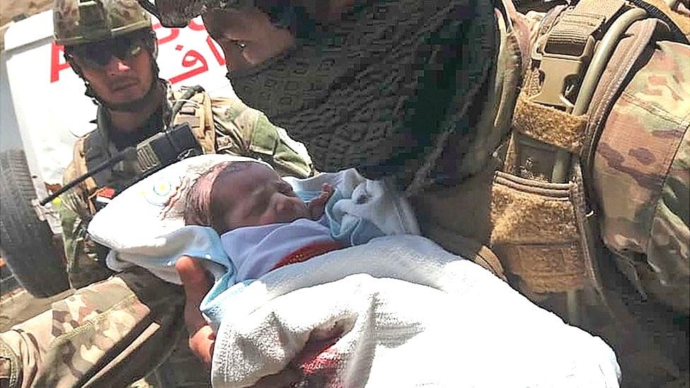 An Afghan security personnel carries a newborn baby from a hospital, at the site of an attack in Kabul on May 12, 2020.