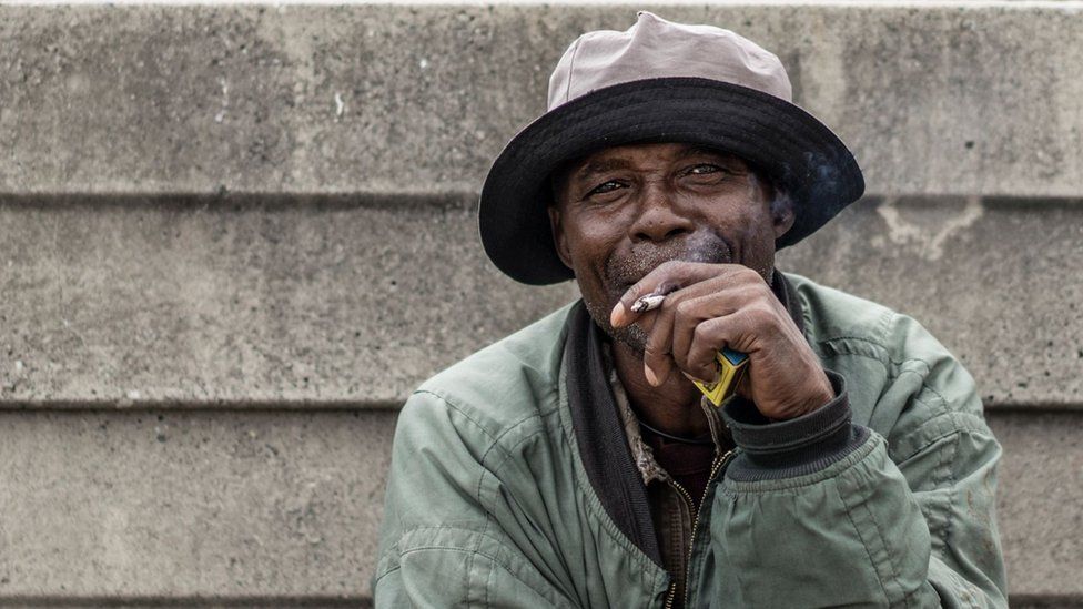 Lesotho miner Francis Malise, 60, smokes in the yard of the Kroondal Circle Labour Hostel, in Rustenburg on April 25, 2017.