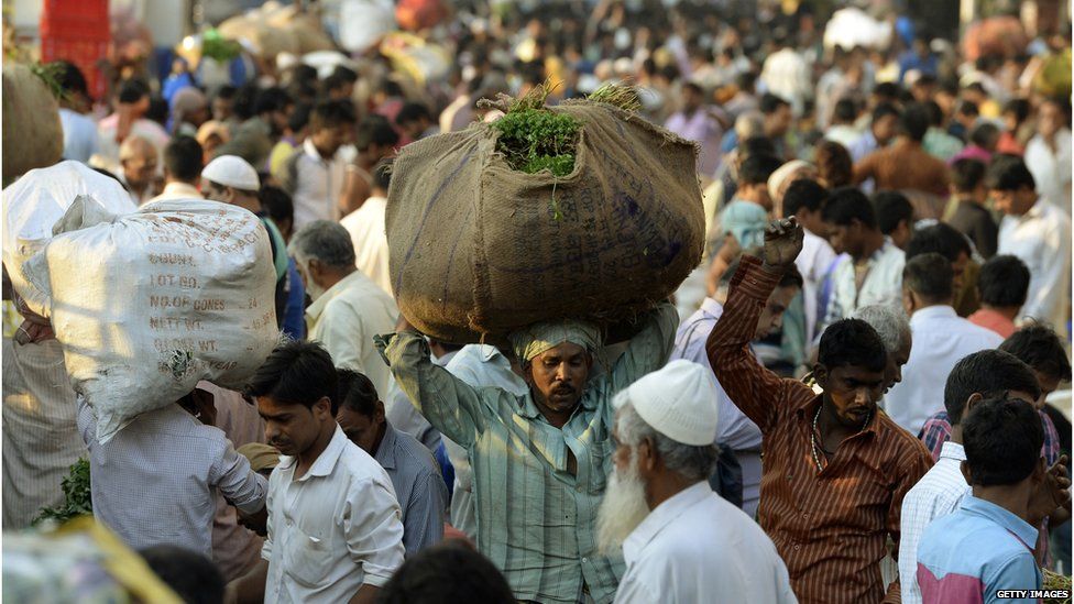 Man in a crowd carrying large package on his head in Mumbai