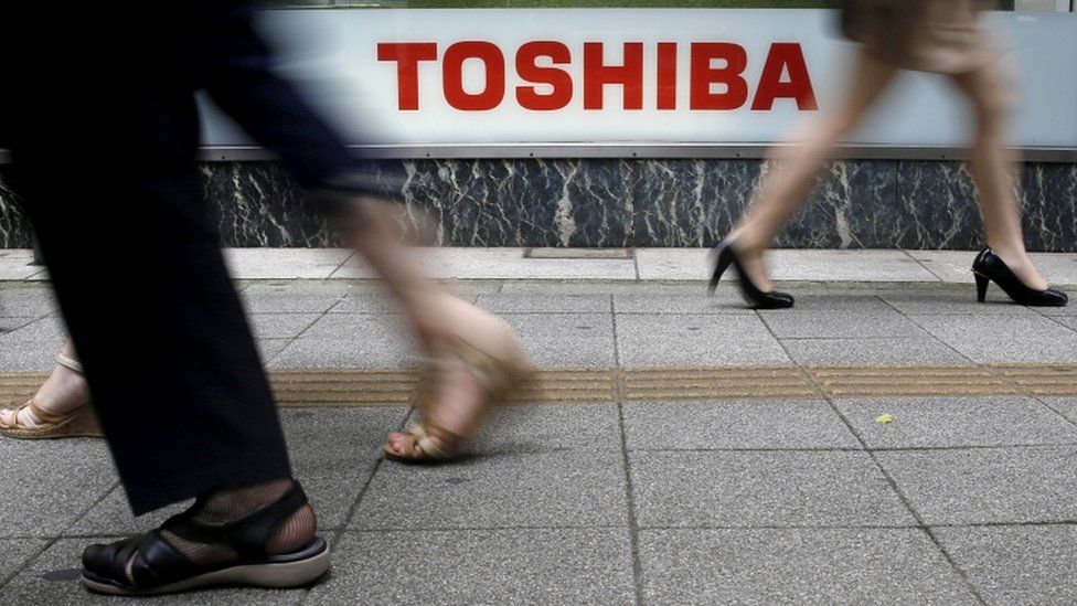 Пешеходы проходят мимо логотипа Toshiba Corp у магазина электроники в Токио.