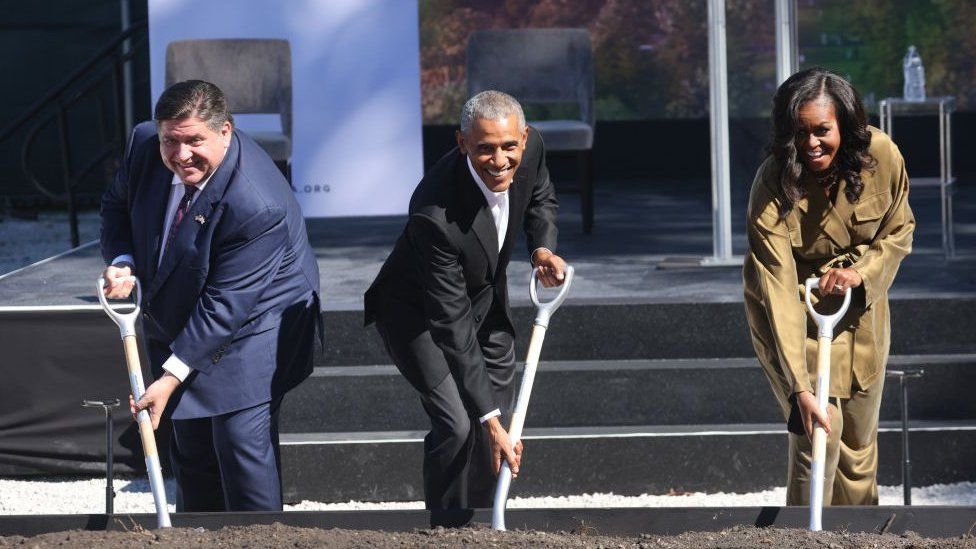 Губернатор Иллинойса Дж. Б. Притцкер копает грязь на площадке во время торжественной церемонии закладки фундамента с Бараком и Мишель Обамой