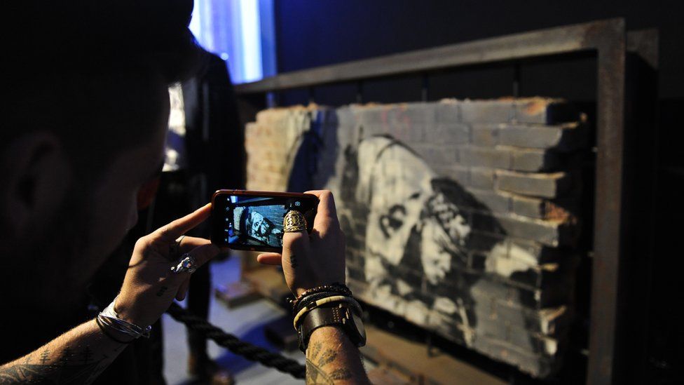 A picture of Banksy's Snorting Copper being taken on a smartphone