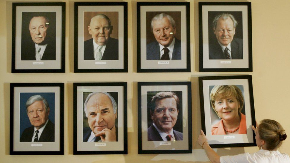 A manager at Berlin's Kanzelreck restaurant puts a photo of Angela Merkel next to her predecessors