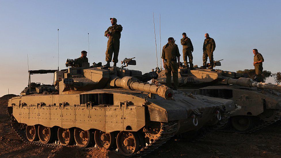 Israeli soldiers stand on tanks deployed on the southern border with the Gaza Strip on 29 November 2023