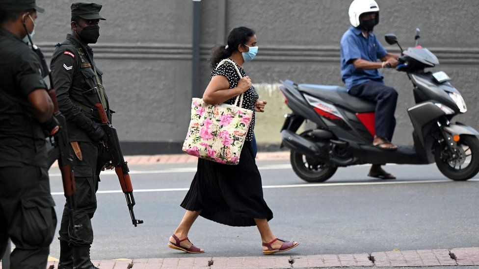 A pedestrian walks past soldiers standing on guard along a street in Colombo on April 2, 2022