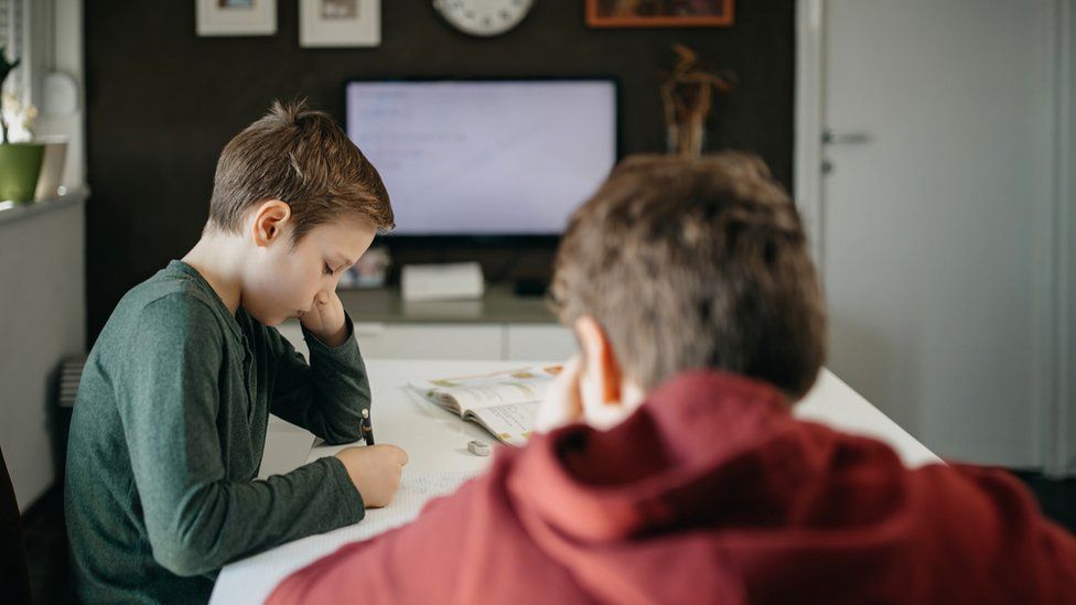 Boys working at table with TV in background