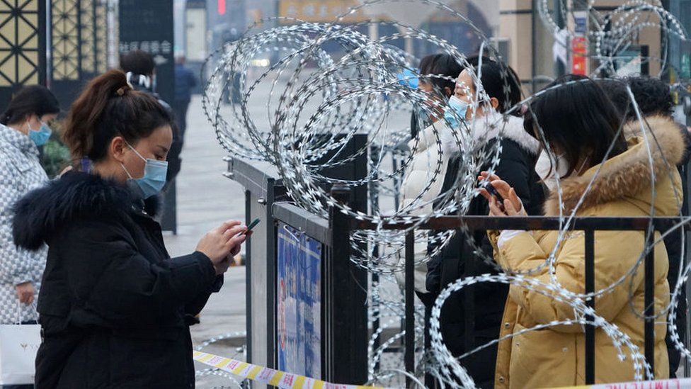 Жители Сианя стоят у ворот с колючей проволокой на своих мобильных