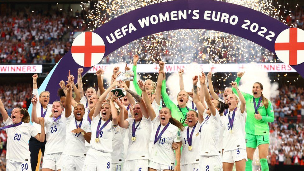 England's Leah Williamson and Millie Bright lift the trophy, in front of a sign with England flags and sparklers, as they celebrate winning the Women's Euro 2022