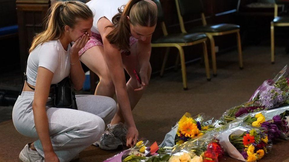 Two women putting down floral tributes at a vigil at St Peter's church in Nottingham.