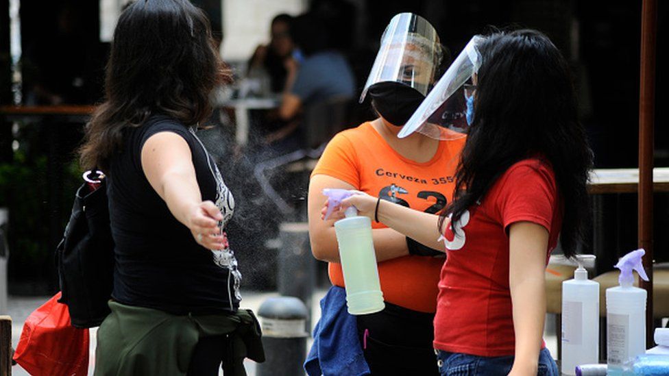A hostess wears face shield while sprays antibacterial solution to a person before she enters in a restaurant of Zona rosa in Mexico City