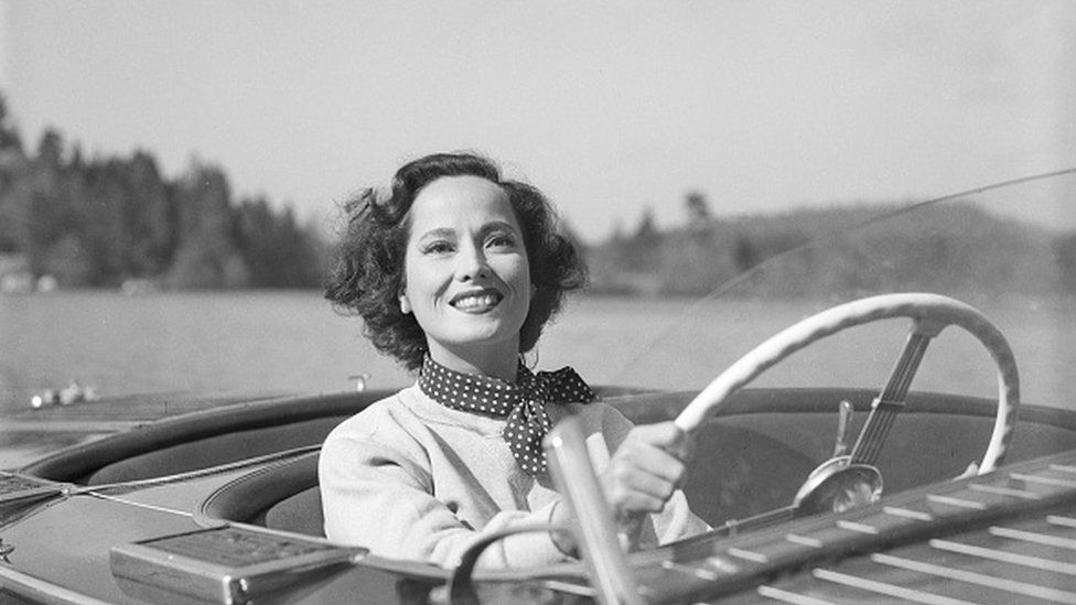 Merle Oberon seen behind the wheel of a motorboat in her film Night Song