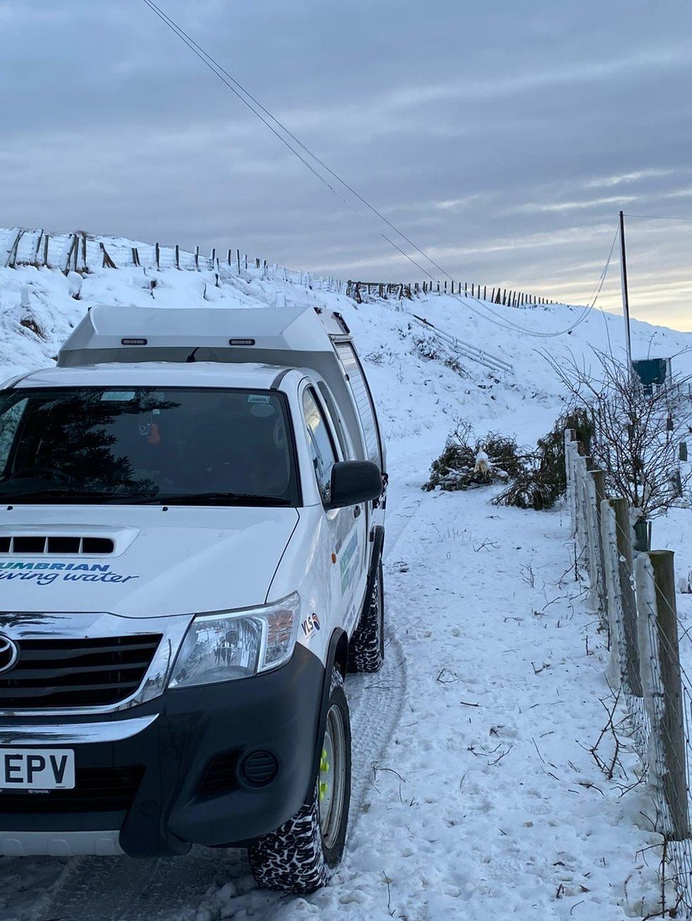 A Northumbrian Water van parked in the snow near a fallen tree