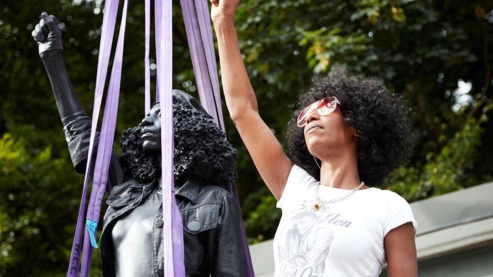 Jen Reid poses next to a sculpture by Marc Quinn portraying her, titled "A Surge of Power (Jen Reid) 2020", in Bristol,