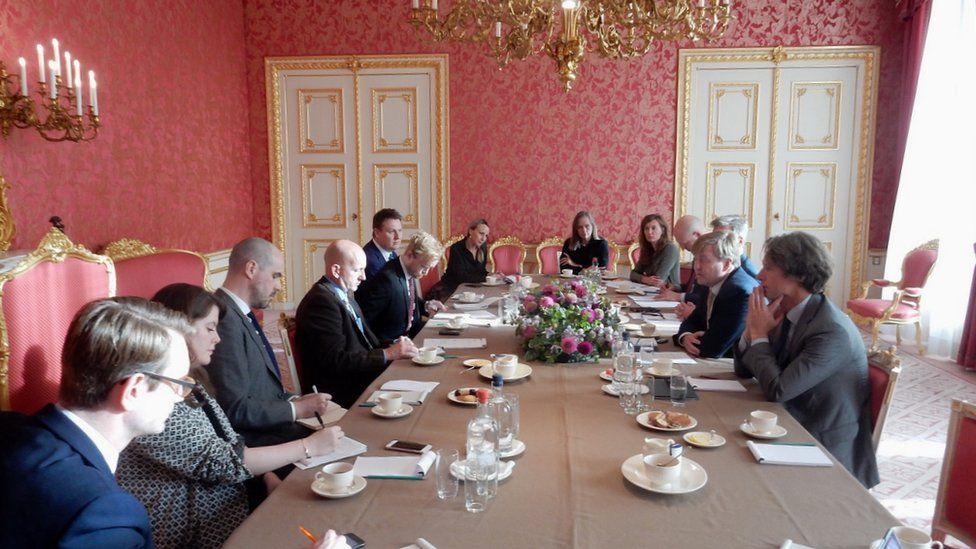 Journalists sit around a table in a grand setting of the Dutch royal palace, with the king in their midst