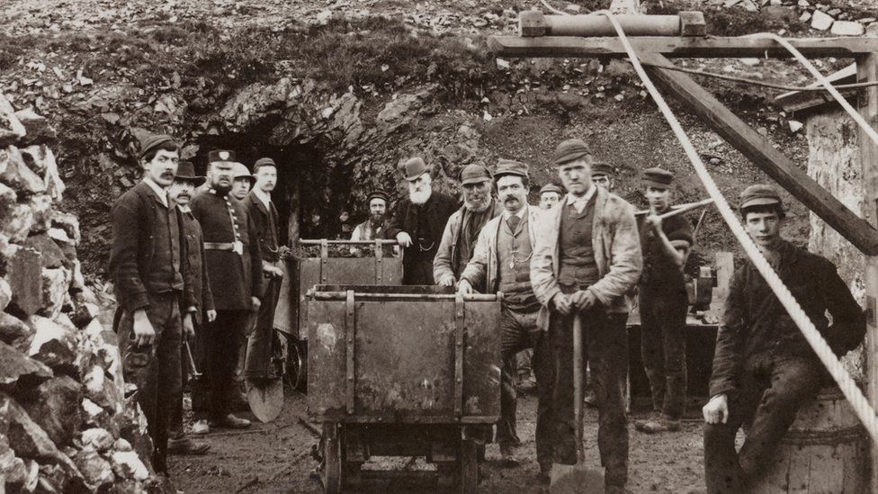 Black and white photos shows a dozen workers outside mine entrance