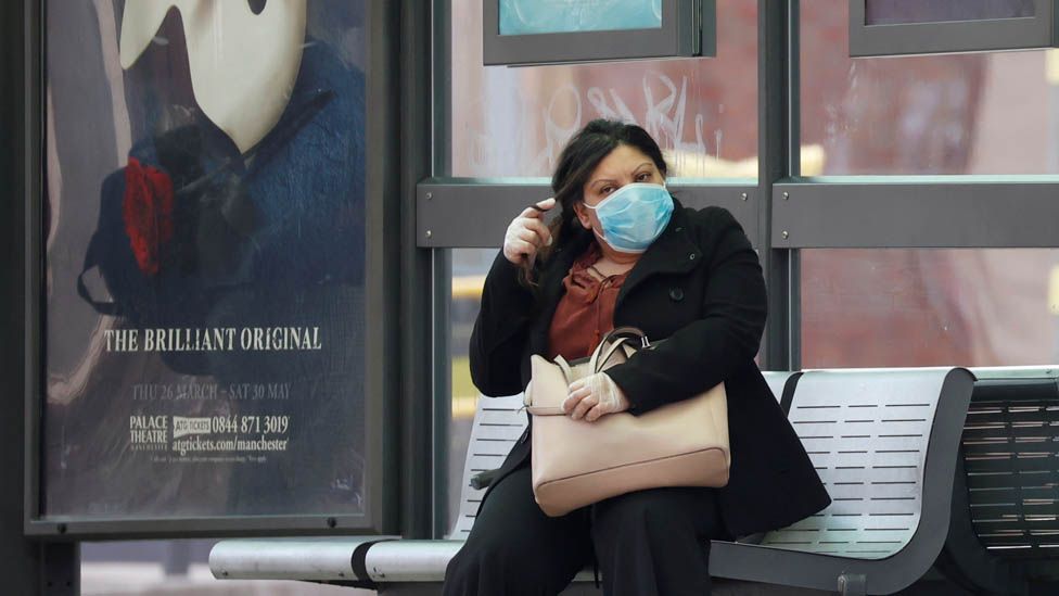 A woman wearing a protective face mask is seen waiting for a bus in Manchester, following the outbreak of the coronavirus disease