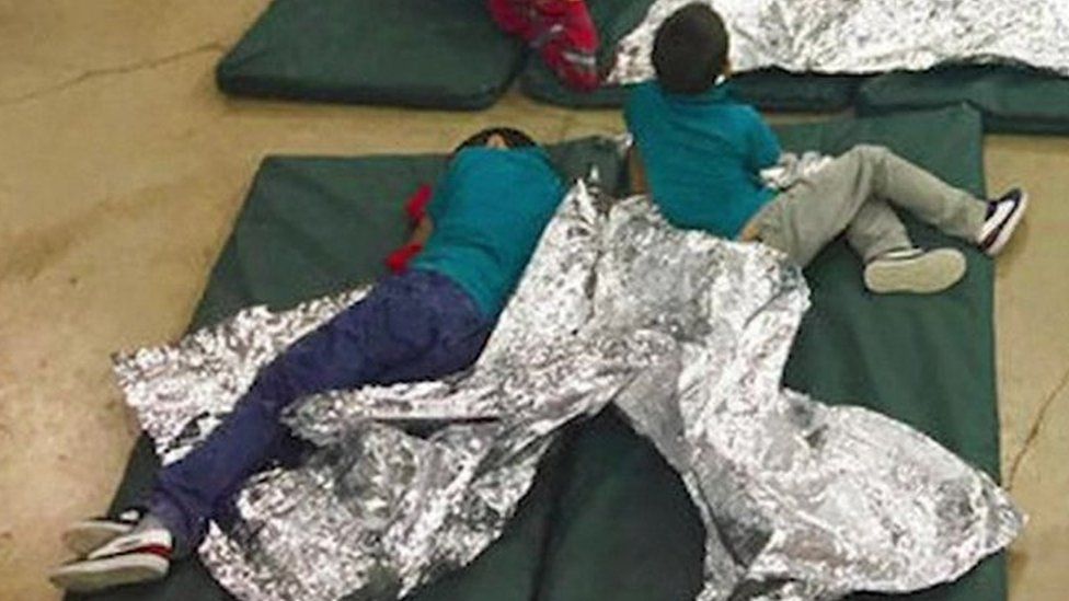 Three boys lie on thin green mattresses on the floor covered in foil blankets