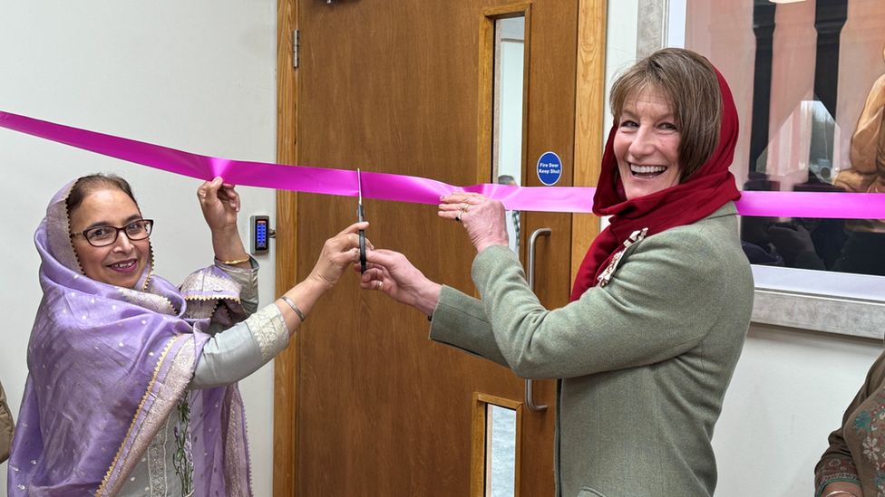 Two women smiling and cutting a ribbon