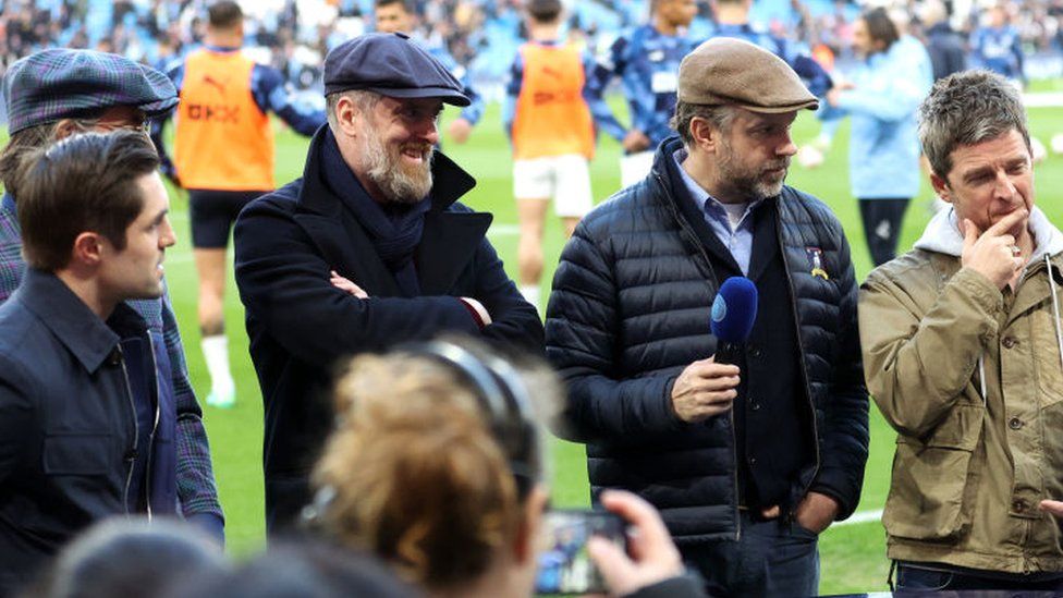 (L-R) Actors Phil Dunster, James Lance, Brendan Hunt and Jason Sudeikis from the television show Ted Lasso and Noel Gallagher are interviewed prior to the Premier League match between Manchester City and Arsenal