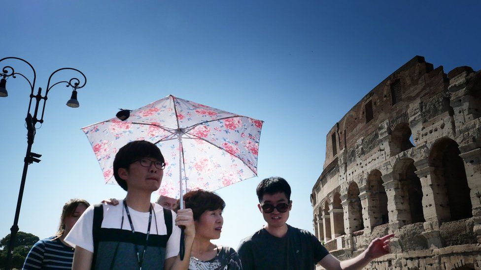 Tourists shelter from the sun with umbrellas in front of the Colosseum in Rome on June 25, 2019 during a heatwave.