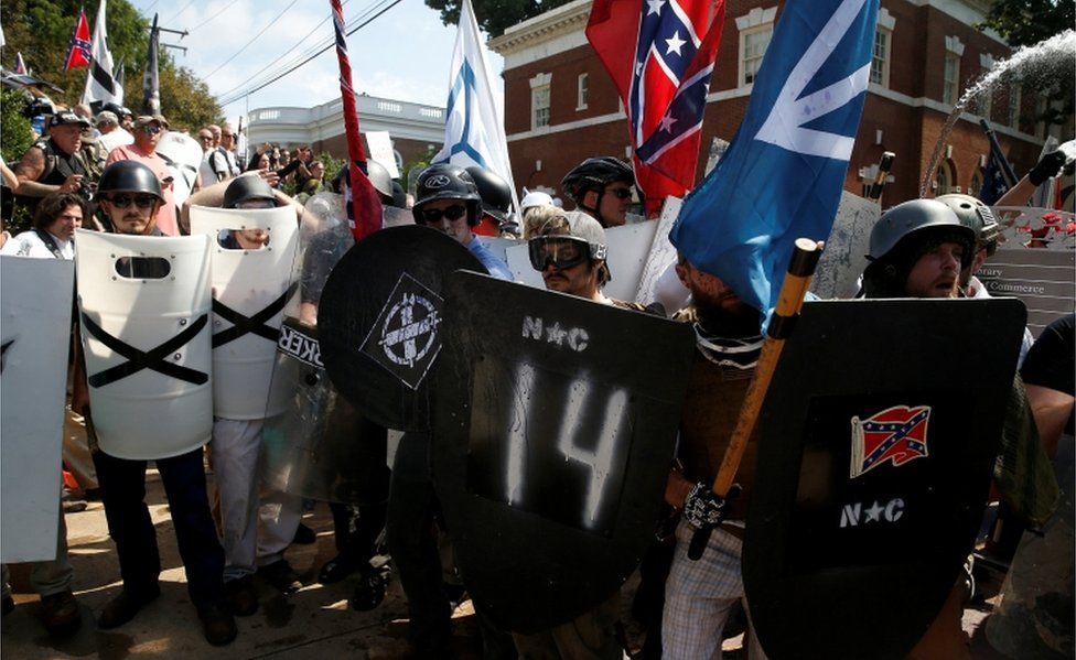 White supremacists in helmets and sunglasses stand behind their spray-painted shields