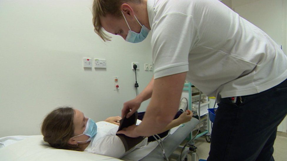 Patient Sophia lies on a bed while she has a blood pressure cuff secured by physiotherapist James.
