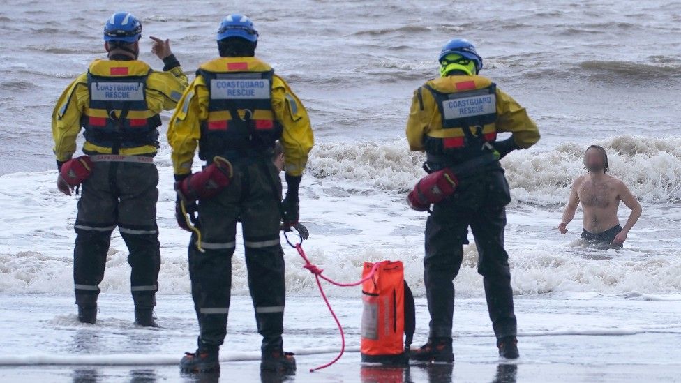 A coastguard search and rescue team ask a swimmer to come out of the sea in New Brighton