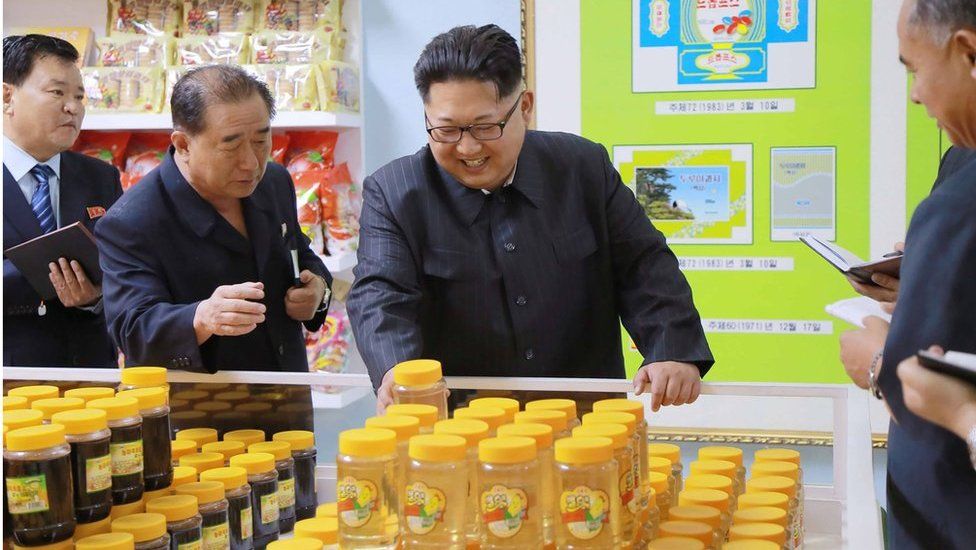 Image released by KCNA on 16 June 2016 showing North Korean leader Kim Jong-un (centre) surrounded by other officials taking notes, as he smilingly inspects products in the Pyongyang cornstarch factory.