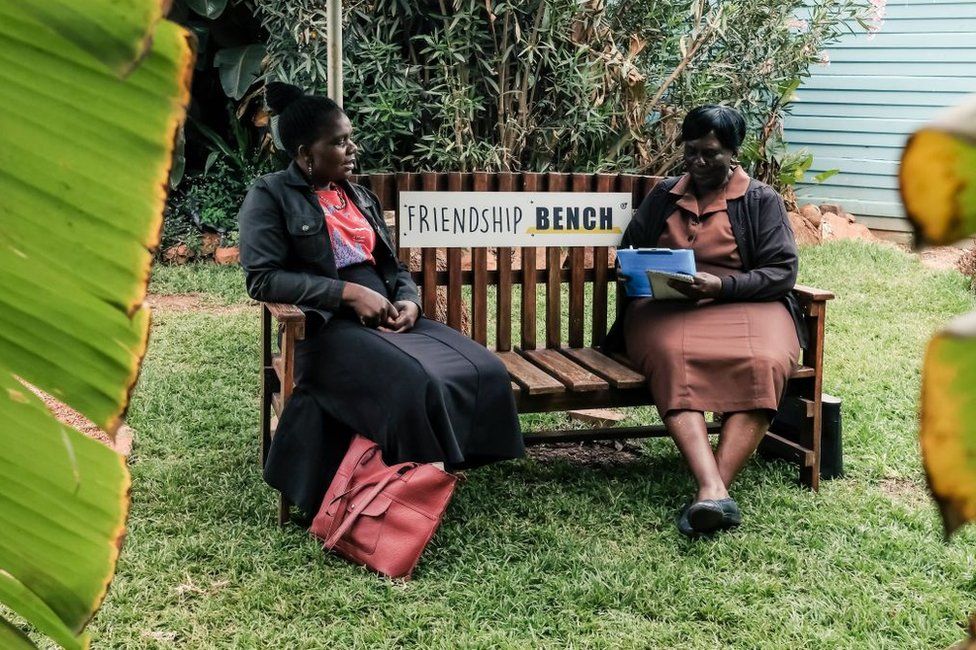 Counsellor "Gogo" Shery Ziwakayi (R) sits on a bench in conversation with a client "Muzukuru" Choice Jiya (L) during a private counselling session at the Friendship Bench in Harare on November 4, 2022. - A Zimbabwean doctor has come up with a novel way of providing desperately needed, yet free mental health therapy for Zimbabweans using elderly lay health workers referred to as grandmothers. Dubbed the Friendship Bench, psychiatry professor Dixon Chibanda's creation is a wooden park bench where people experiencing common mental disorders such as anxiety and depression sit and receive therapy from grandmothers. Now the model is temporarily being exported to FIFA World Cup in Qatar later this month to cast the spotlight on mental health. The Friendship Bench in partnership with the World Health Organisation (WHO) will set up 32 friendship benches at various spots in Qatar, each representing the competing teams.