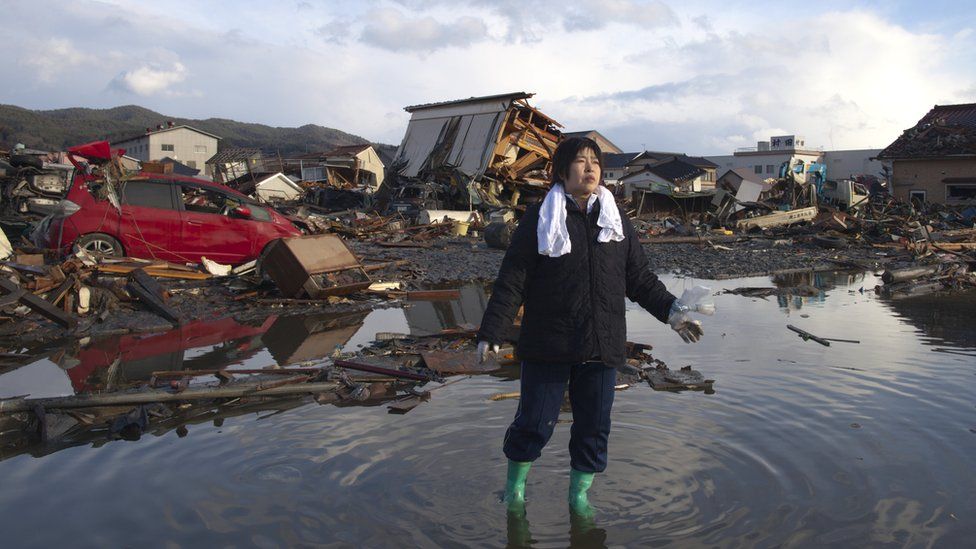 A woman stands in water amidst tsunami wreckage