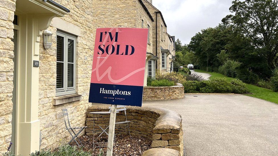 A 'sold' sign outside a traditional stone Cotswold property