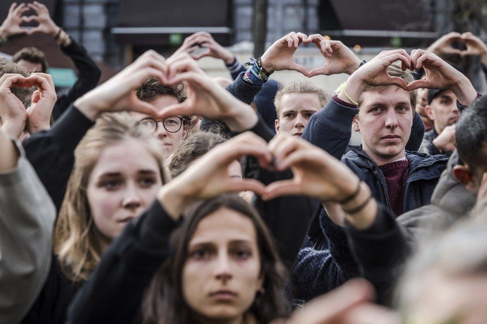 People make the shape of a heart with their hands as they stand for a moment of silence at the Bourse during the one-year anniversary for Brussels attacks victims in Brussels, 22 March