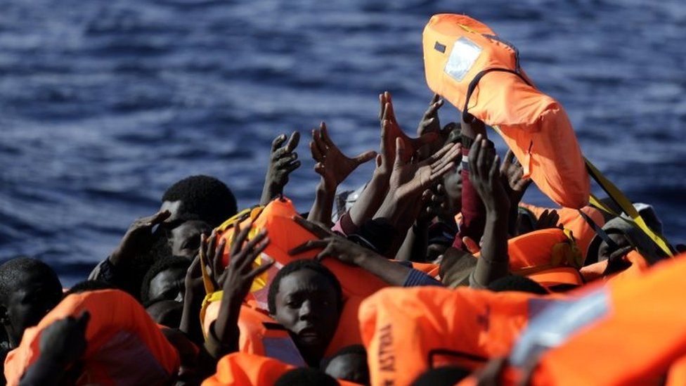 Migrants raise their hands to grab a life jacket on a boat off Libya's coast. Photo: 2 February 2017