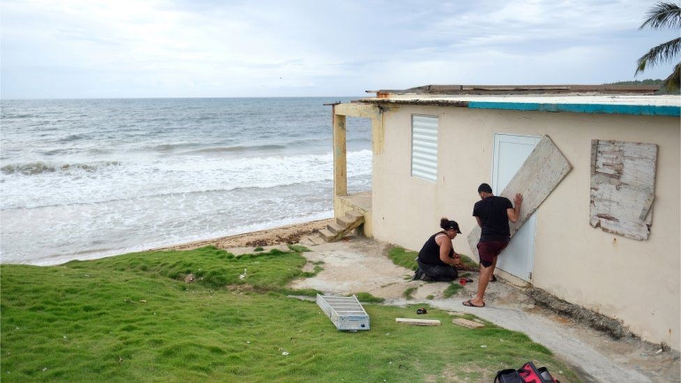 A couple board up the door of their beachfront house as Tropical Storm Dorian approaches in Yabucoa, Puerto Rico