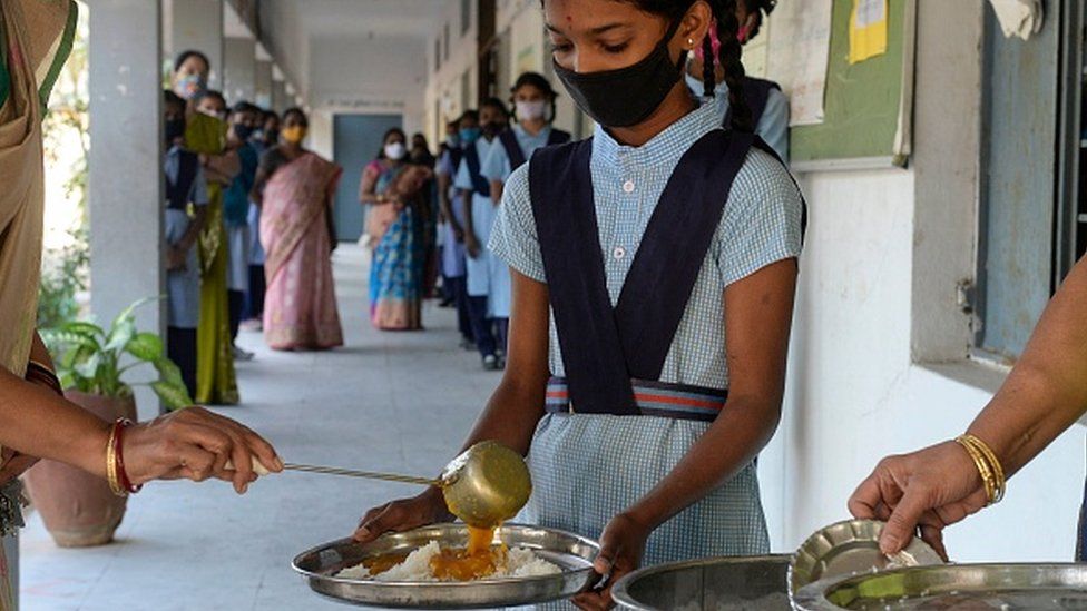 Teachers serve mid-day meal to students during lunch break