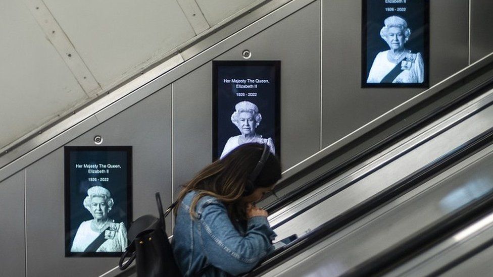 Woman on tube with images of the Queen behind her