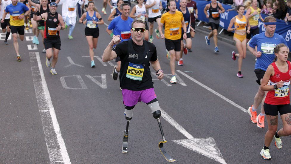 A man with prosthetic legs runs surrounded by other people