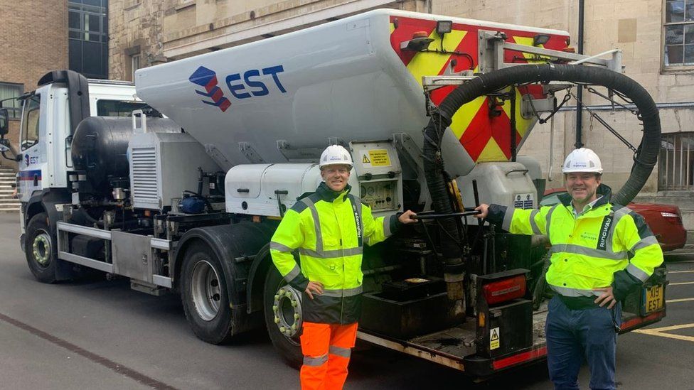 Two men in high vis standing next to a big lorry