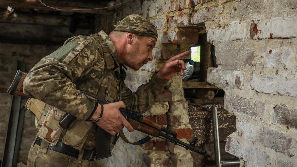 A Ukrainian soldier holds a gun and points forward